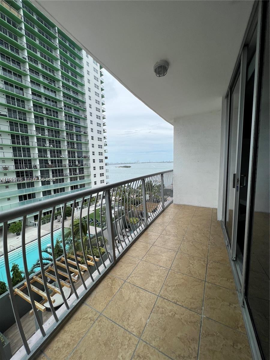 A balcony with tiled flooring overlooks a swimming pool, a neighboring high-rise building, and water — 1750 N Bayshore Dr # 1507, Miami FL 33132, MIAMI, FL