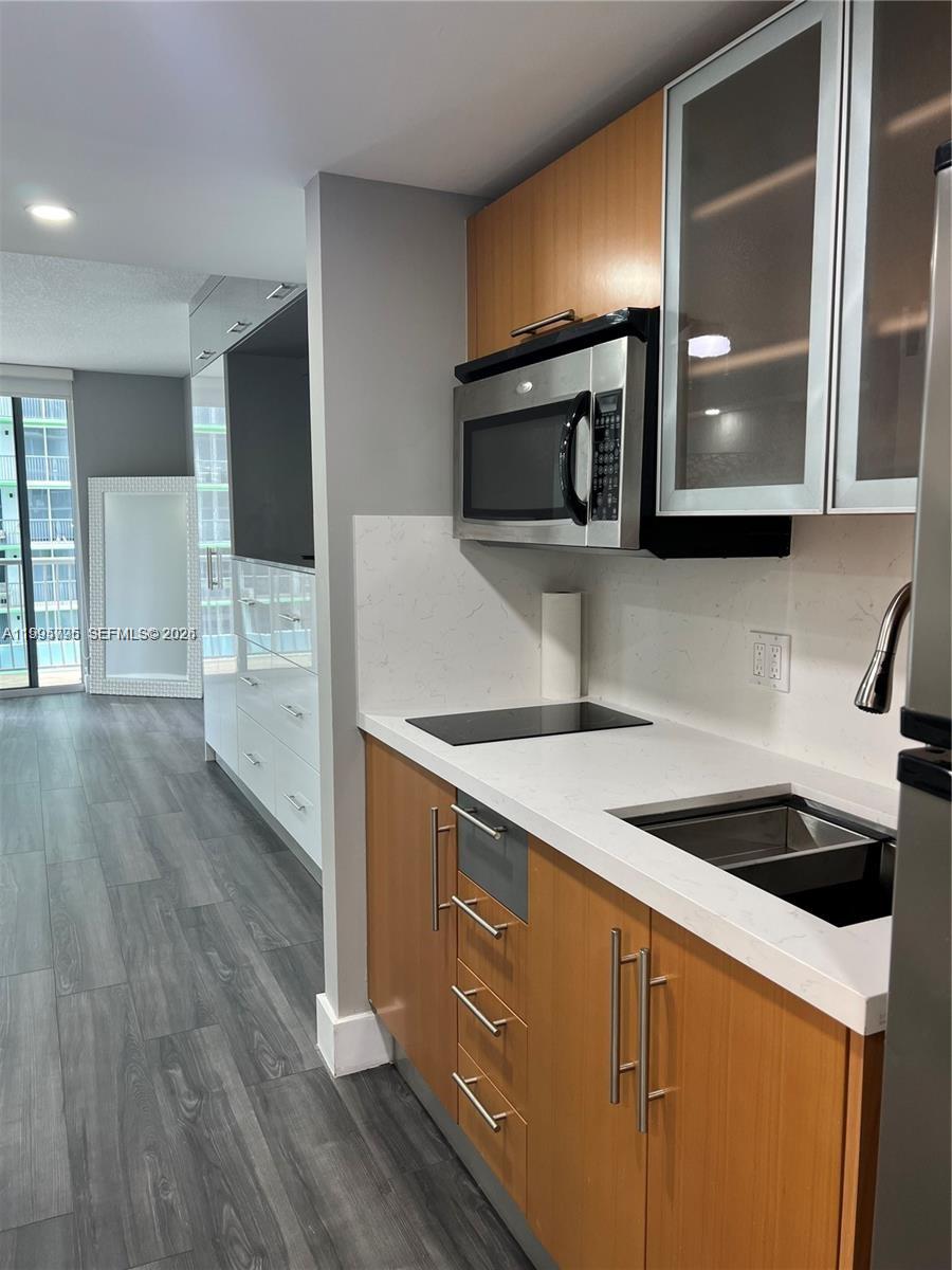 A kitchen features wood cabinets, white countertops, stainless steel appliances, and gray wood-look flooring — 1750 N Bayshore Dr # 1507, Miami FL 33132, MIAMI, FL