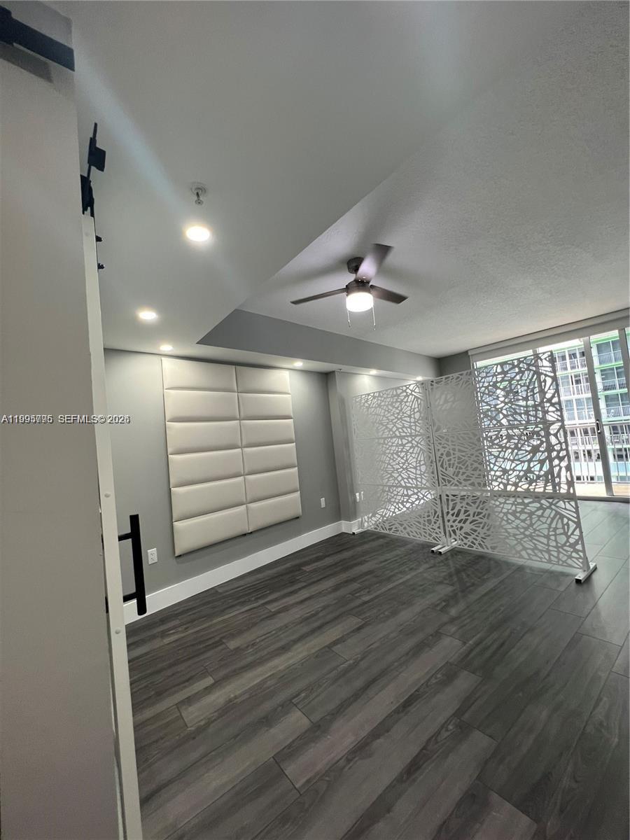 A room with gray wood-look flooring, a ceiling fan, a wall-mounted headboard, and decorative screens — 1750 N Bayshore Dr # 1507, Miami FL 33132, MIAMI, FL