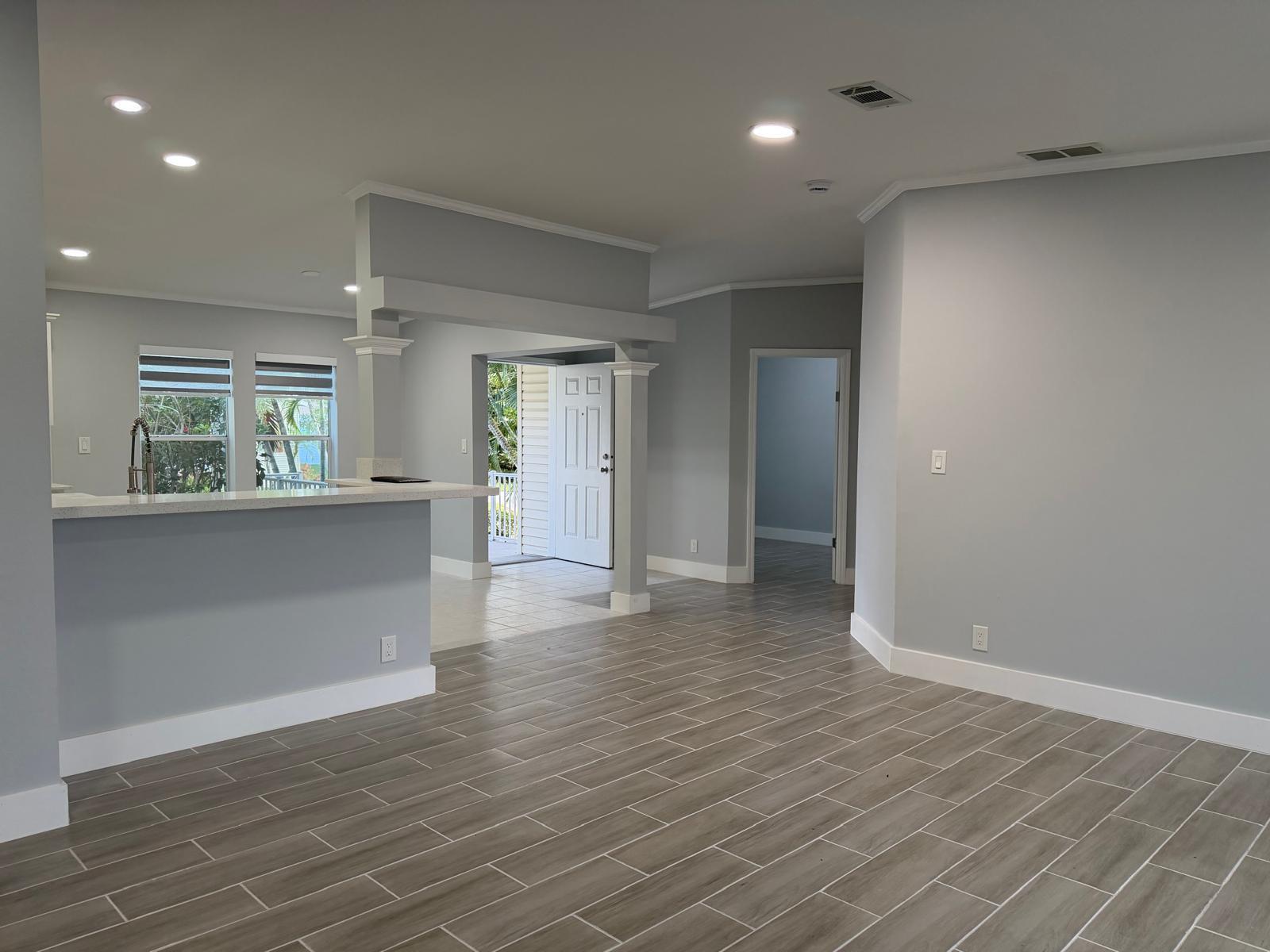 An open-concept living area features gray walls, wood-look tile flooring, and a kitchen breakfast bar — 4165 3rd Court, Atlantis FL 33462, ATLANTIS, FL