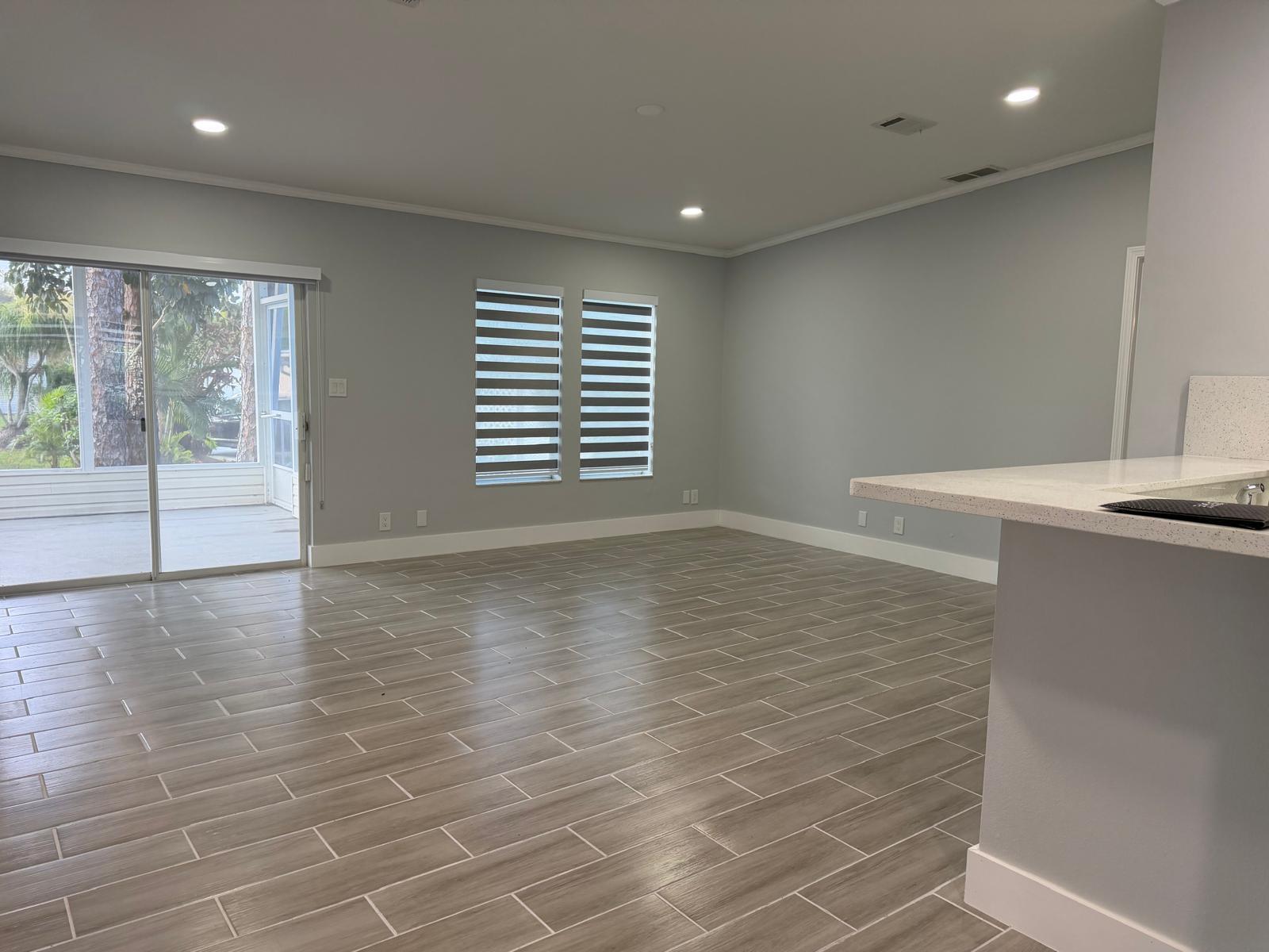 An empty living room with gray walls, wood-look tile flooring, and a sliding glass door — 4165 3rd Court, Atlantis FL 33462, ATLANTIS, FL