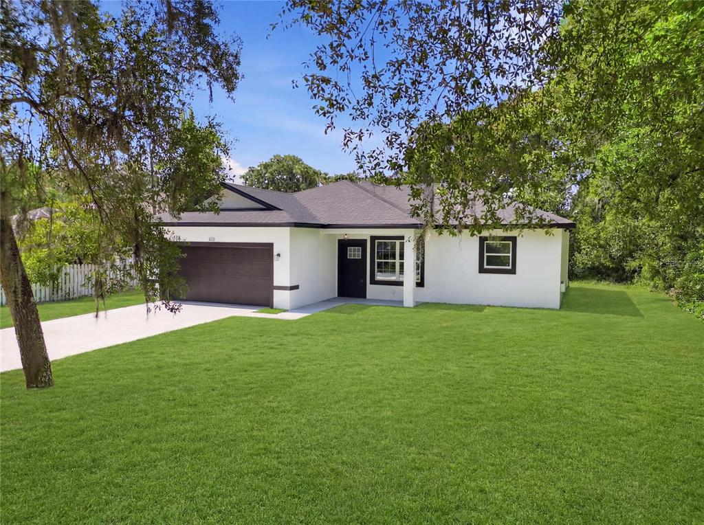 A single-story house with a white stucco exterior, dark trim, and a two-car garage — 881 W WISCONSIN AVENUE, ORANGE CITY, FL