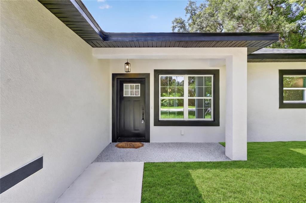 The exterior of a house features a white stucco wall, a black door, and a window — 881 W WISCONSIN AVENUE, ORANGE CITY, FL