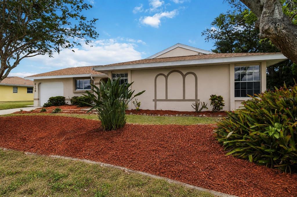 A single-story house with a beige exterior, a white garage door, and red mulch landscaping — 4108 ABBOTSFORD STREET, NORTH PORT, FL