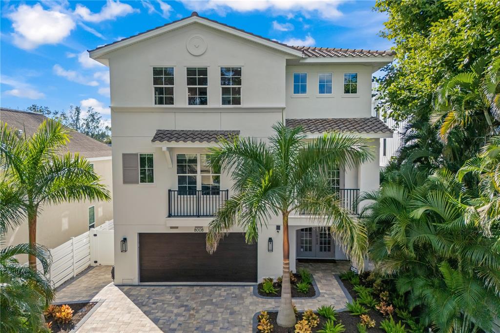 A three-story house with a dark garage door, a palm tree, and a paved driveway — 8008 MIDNIGHT PASS ROAD, SARASOTA, FL