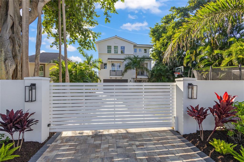 A white horizontal slat gate stands before a three-story house with a paved driveway — 8008 MIDNIGHT PASS ROAD, SARASOTA, FL