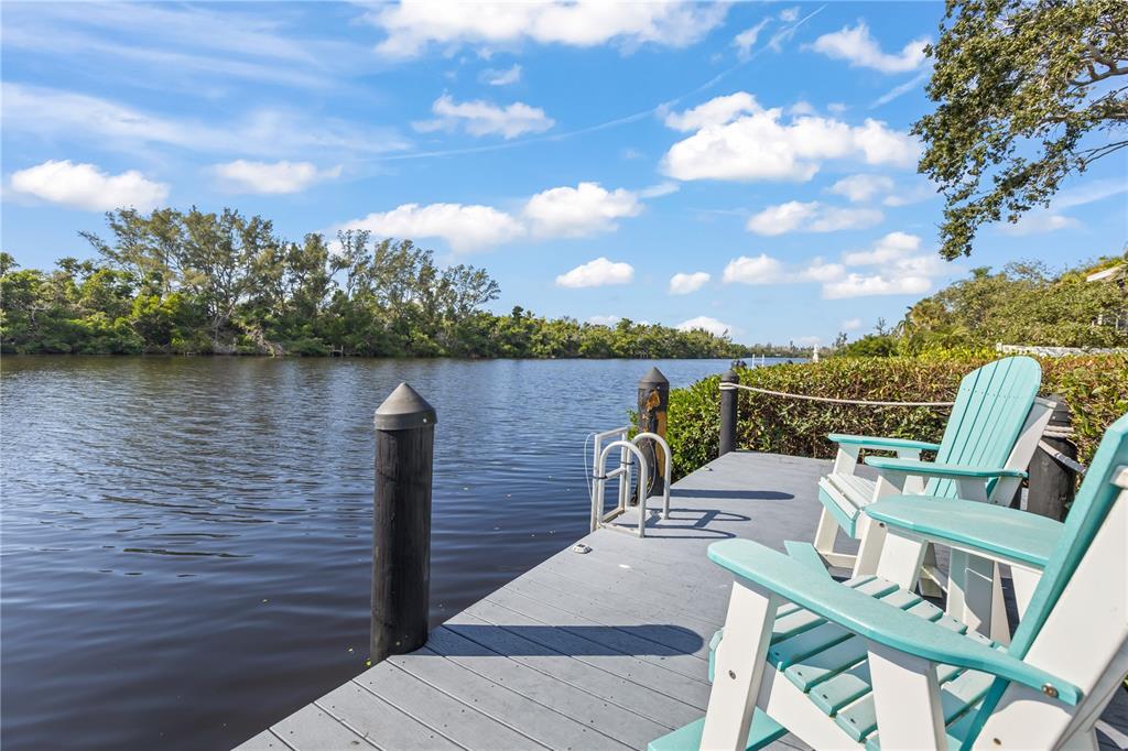 A wooden dock with two chairs overlooks a calm river surrounded by lush green trees — 8008 MIDNIGHT PASS ROAD, SARASOTA, FL