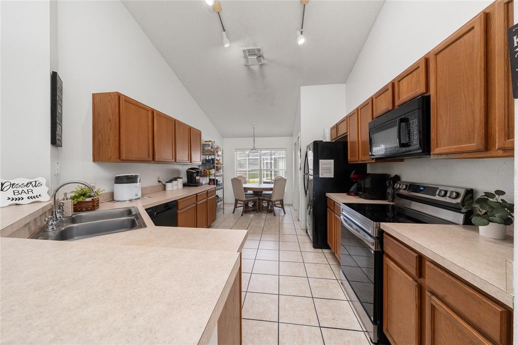 A kitchen with wood cabinets, light countertops, and tile flooring leads to a dining area — 232 LAKE SHORE PARKWAY, DAVENPORT, FL