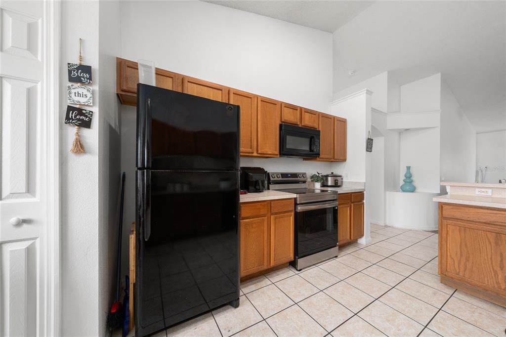 A kitchen features oak cabinets, black and stainless steel appliances, and light-colored tile flooring — 232 LAKE SHORE PARKWAY, DAVENPORT, FL