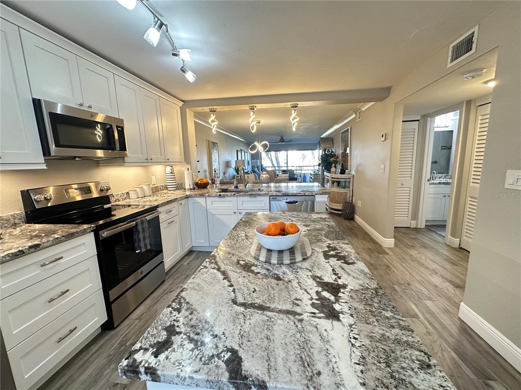 A kitchen features white cabinets, a granite island with a fruit bowl, and wood-look flooring — 106 1ST STREET E UNIT 115, ST PETERSBURG, FL