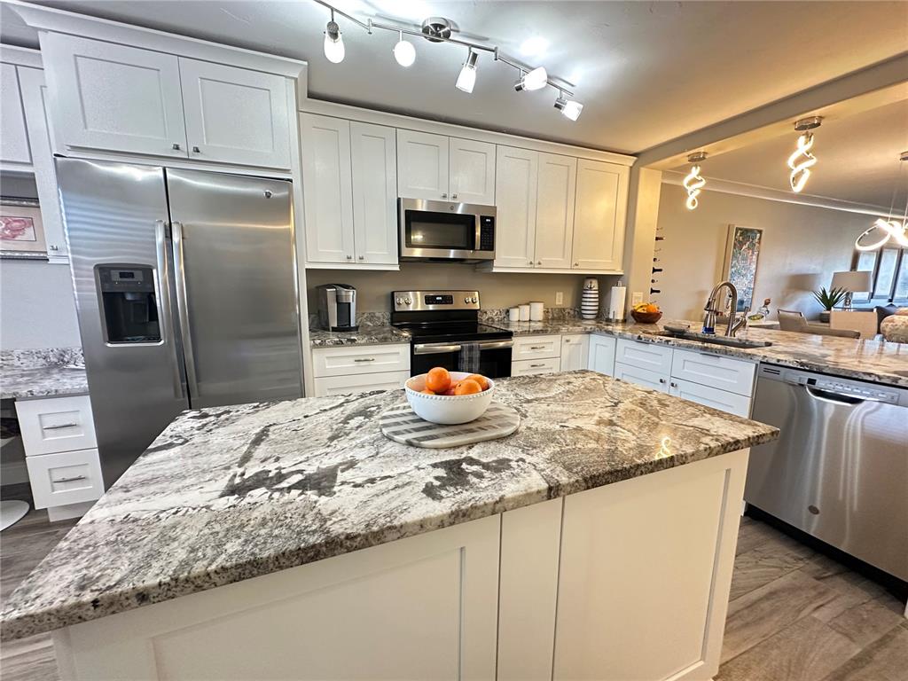 A kitchen features white cabinets, stainless steel appliances, and a large granite-topped island — 106 1ST STREET E UNIT 115, ST PETERSBURG, FL