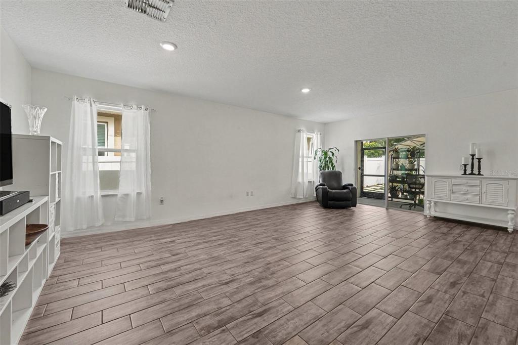 A spacious living room features light wood-look tile flooring, white walls, and a sliding glass door — 1281 WATER WILLOW DRIVE, GROVELAND, FL
