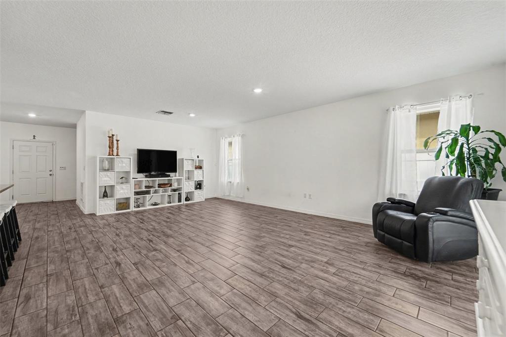 A living room features wood-look tile flooring, white walls, a television console, and a recliner — 1281 WATER WILLOW DRIVE, GROVELAND, FL
