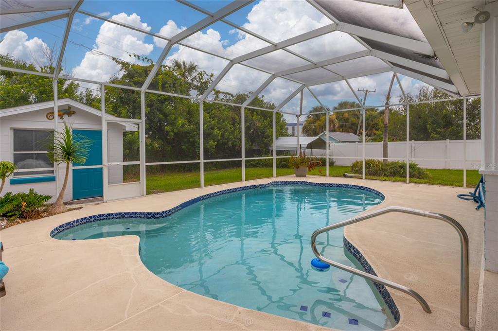 A swimming pool with a metal handrail is enclosed by a screened lanai in a backyard — 1256 BEL AIRE DRIVE, DAYTONA BEACH, FL