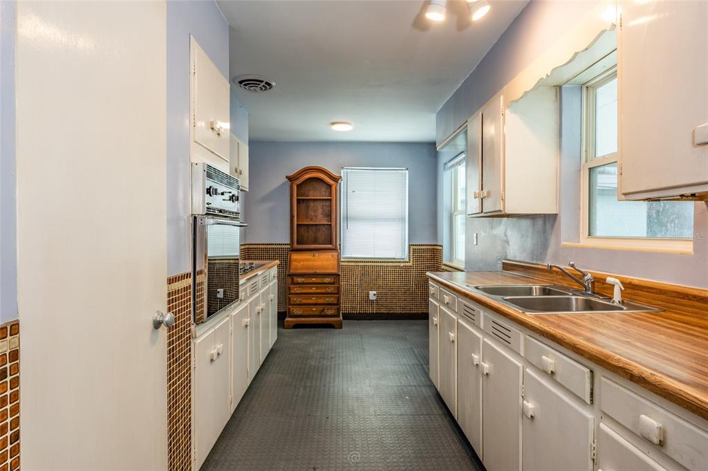 A kitchen features white cabinetry, wood-look laminate countertops, tiled walls, and a vintage wooden hutch — 1256 BEL AIRE DRIVE, DAYTONA BEACH, FL