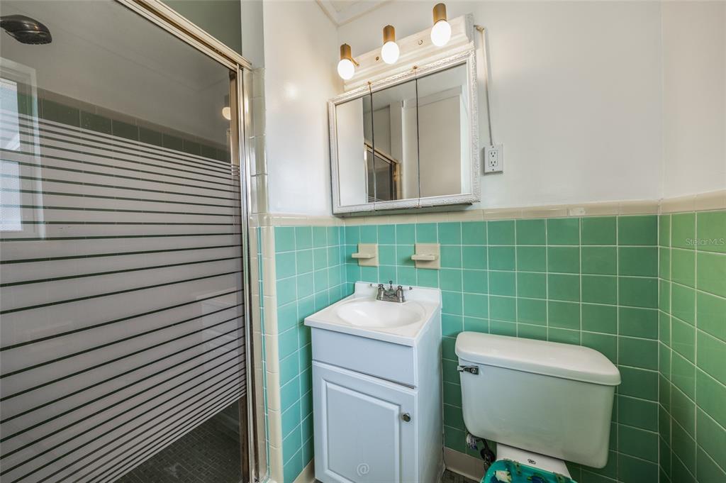 A bathroom with green tiled walls, a white vanity, a medicine cabinet, and a shower — 1256 BEL AIRE DRIVE, DAYTONA BEACH, FL