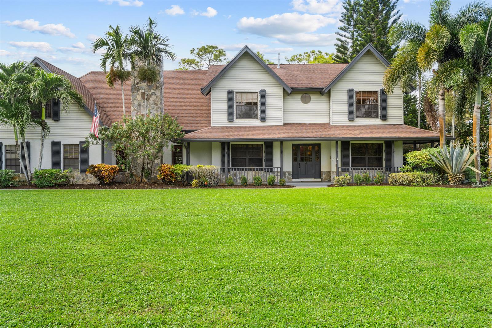 A two-story house with light siding, a stone chimney, and a front porch faces a lawn — 5371 Cougars Prowl, Lake Worth FL 33449, LAKE WORTH, FL