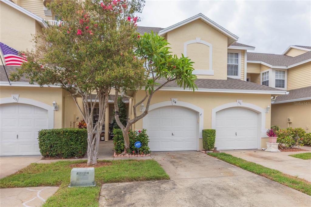 A multi-unit residential building features three garage doors, light-colored stucco walls, and a small tree — 1050 STARKEY ROAD UNIT 104, LARGO, FL