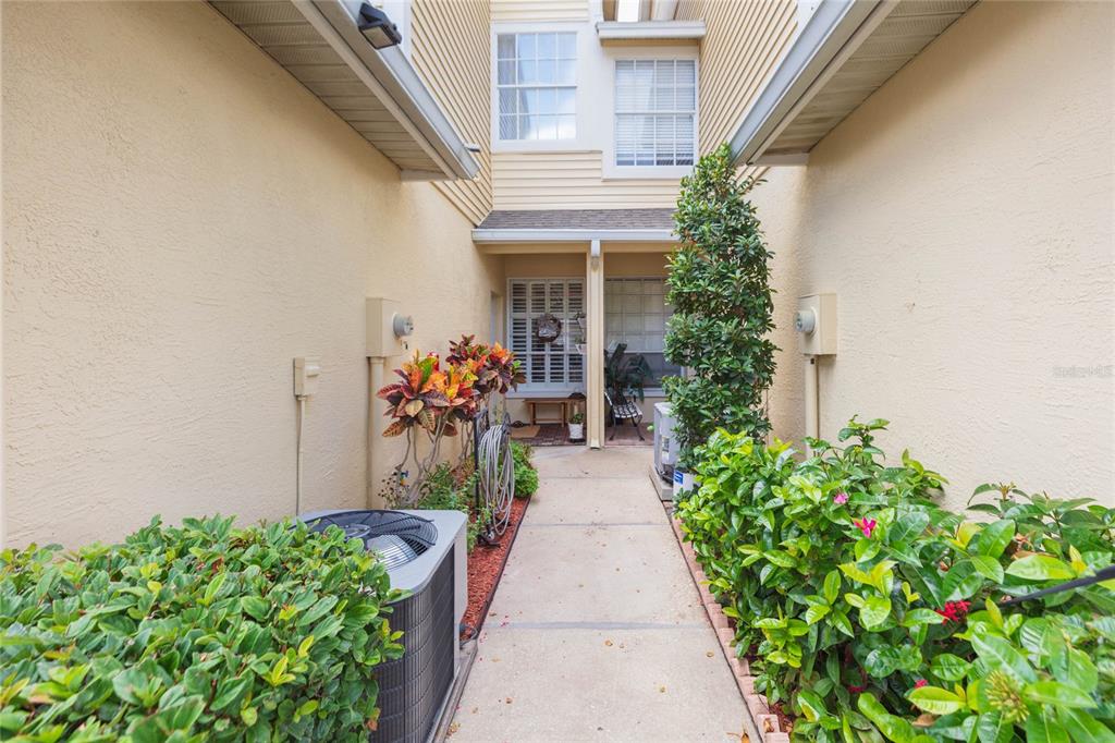 A narrow concrete walkway leads to an entryway between two beige stucco building walls — 1050 STARKEY ROAD UNIT 104, LARGO, FL