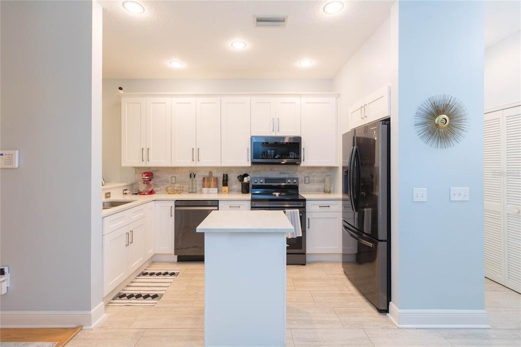 A kitchen features white cabinets, stainless steel appliances, a small island, and light tile flooring — 1050 STARKEY ROAD UNIT 104, LARGO, FL