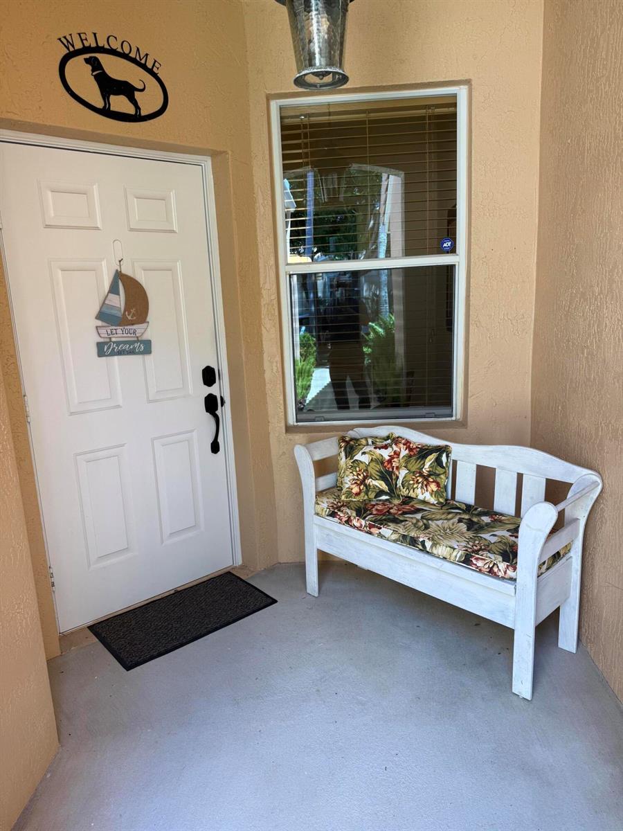 A white front door with a bench sits on a covered entryway porch — 227 Coral Trace Lane # 227, Delray Beach FL 33445, DELRAY BEACH, FL