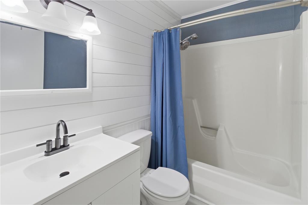 A bathroom features a white vanity, a toilet, and a shower-tub combo with blue curtains — 100 N HIGHLAND AVENUE, GREEN COVE SPRINGS, FL