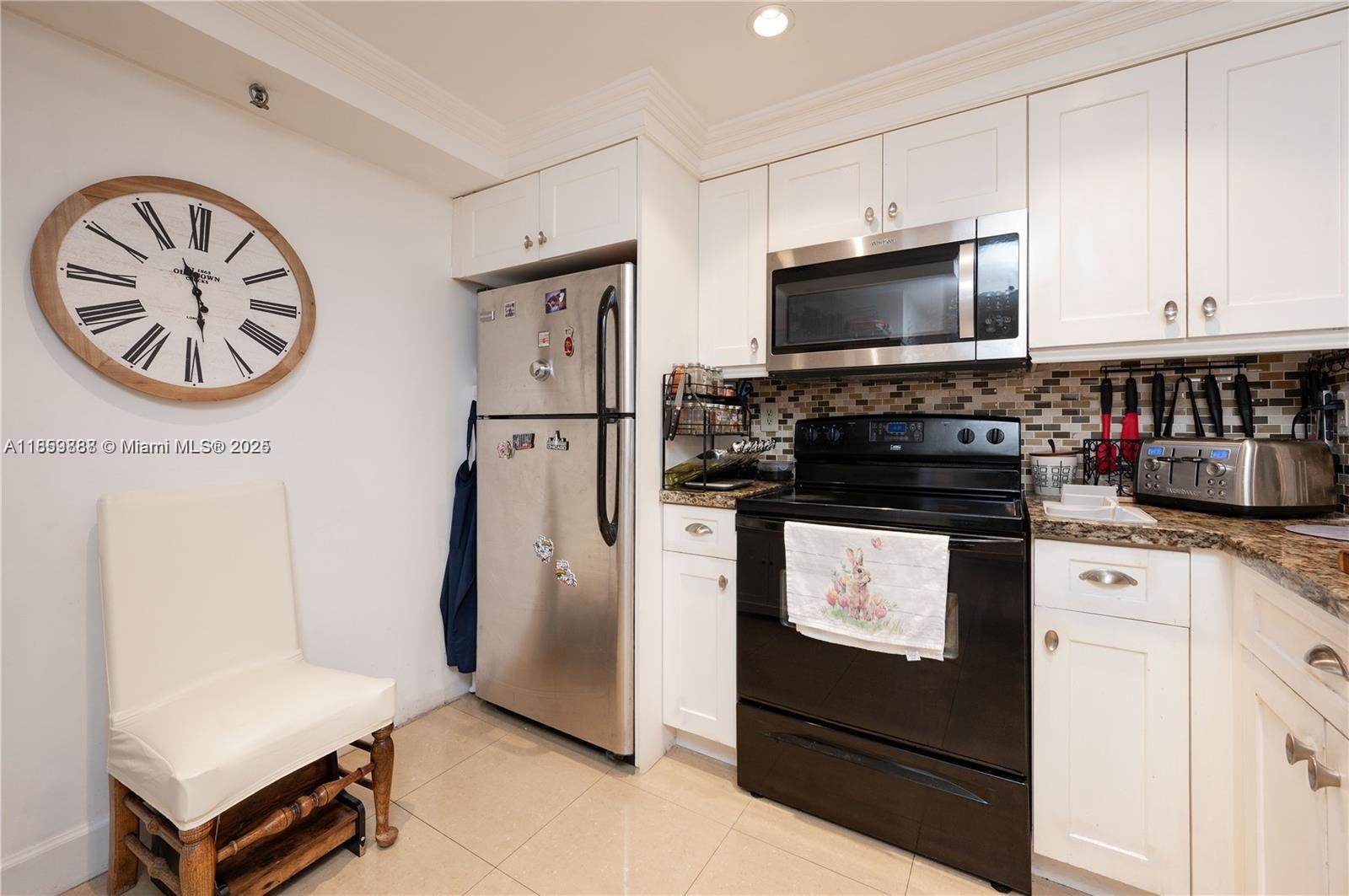 A kitchen features white cabinets, stainless steel appliances, a black stove, and a large wall clock — 1621 Collins Ave # 302, Miami Beach FL 33139, MIAMI BEACH, FL