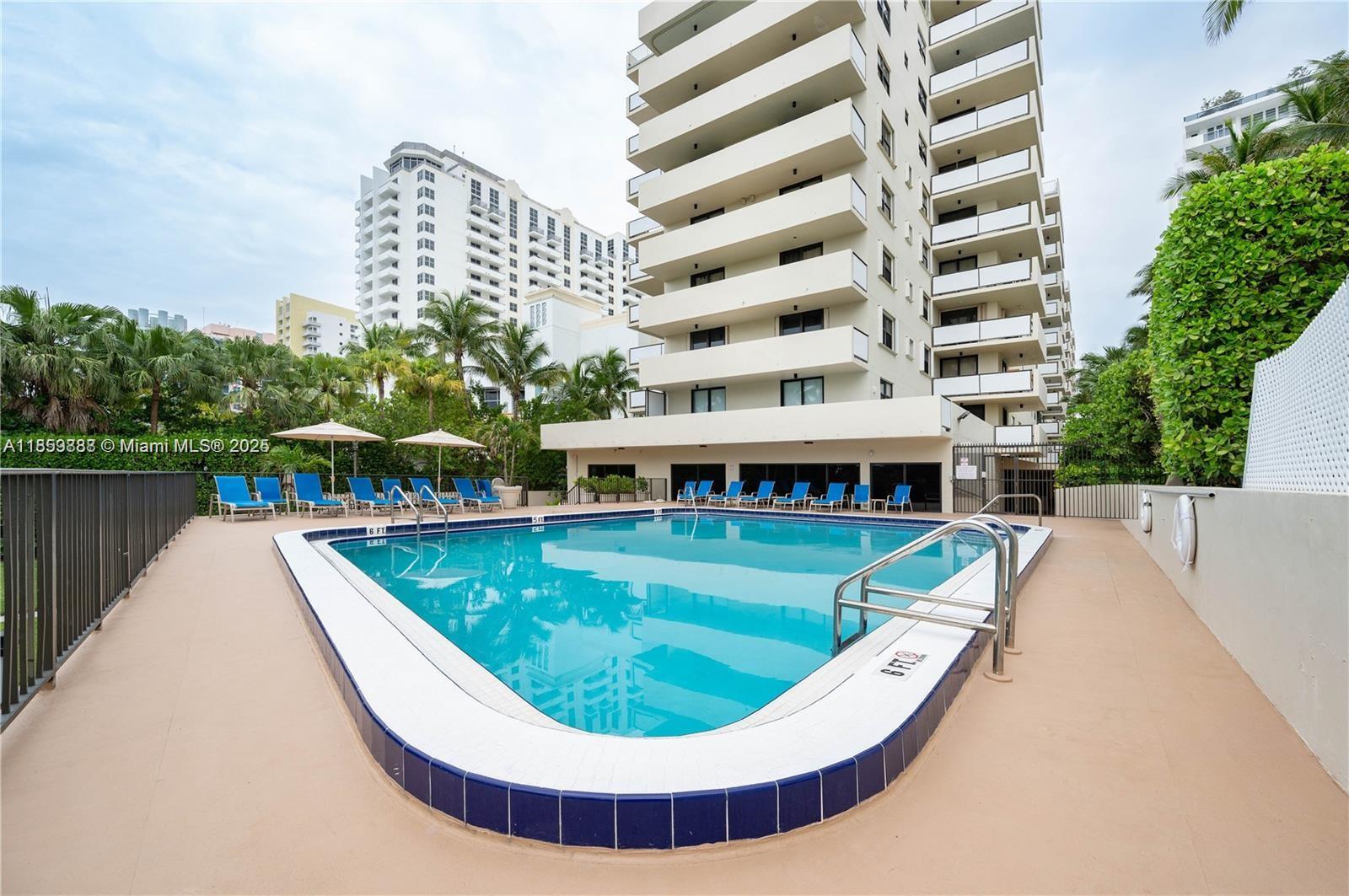 A rectangular swimming pool with blue tiles sits on a patio beside a tall building — 1621 Collins Ave # 302, Miami Beach FL 33139, MIAMI BEACH, FL