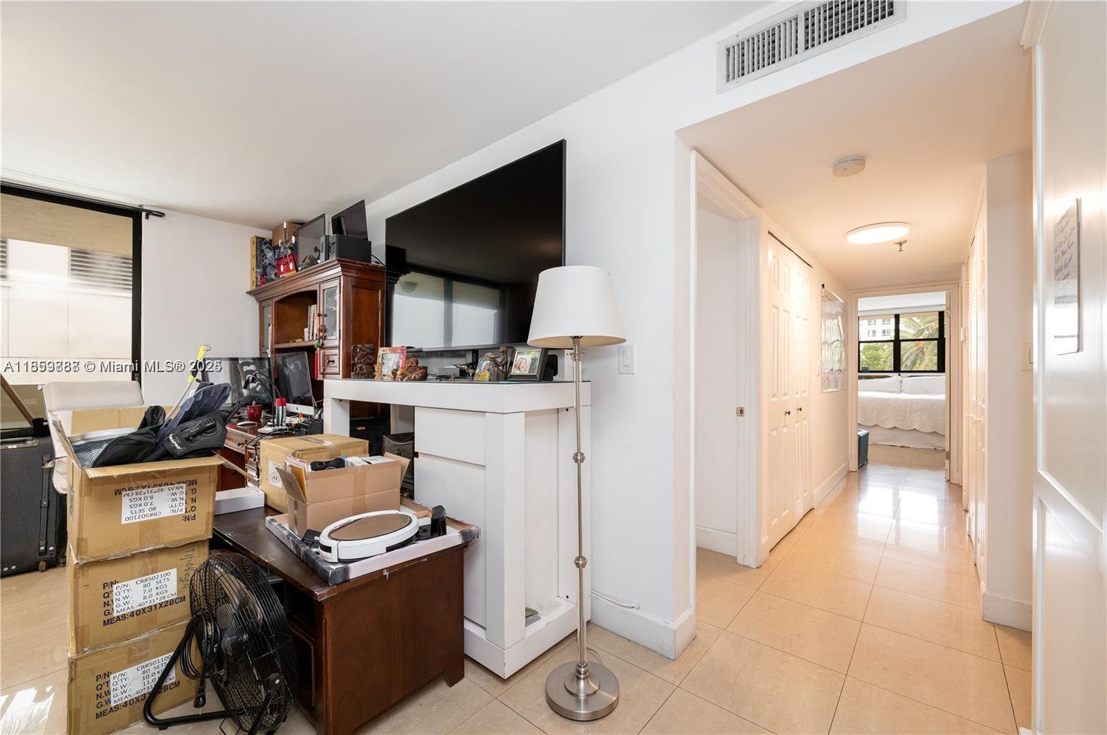 A living area with a television, a floor lamp, and stacked boxes leads to a hallway — 1621 Collins Ave # 302, Miami Beach FL 33139, MIAMI BEACH, FL