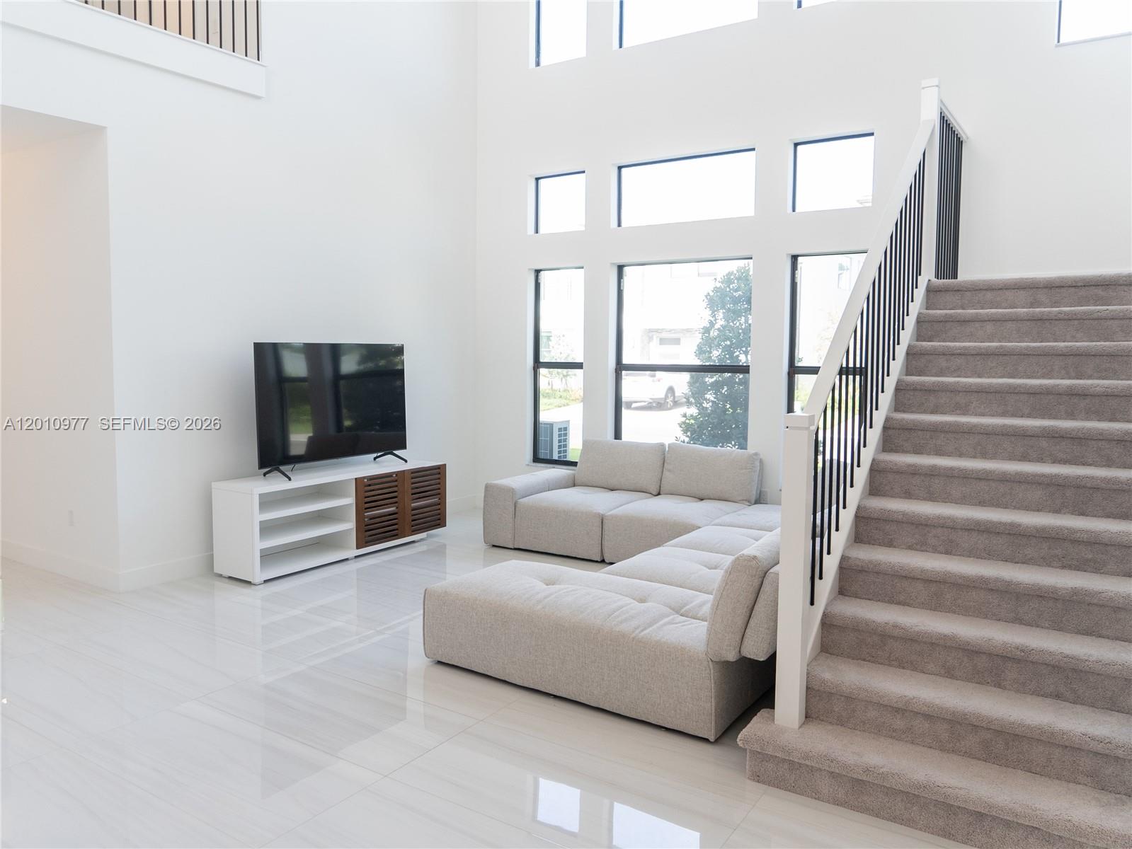 A living room features a sectional sofa, a television console, and stairs with carpeted steps — 8151 Laurel Falls Dr, Boca Raton FL 33496, BOCA RATON, FL