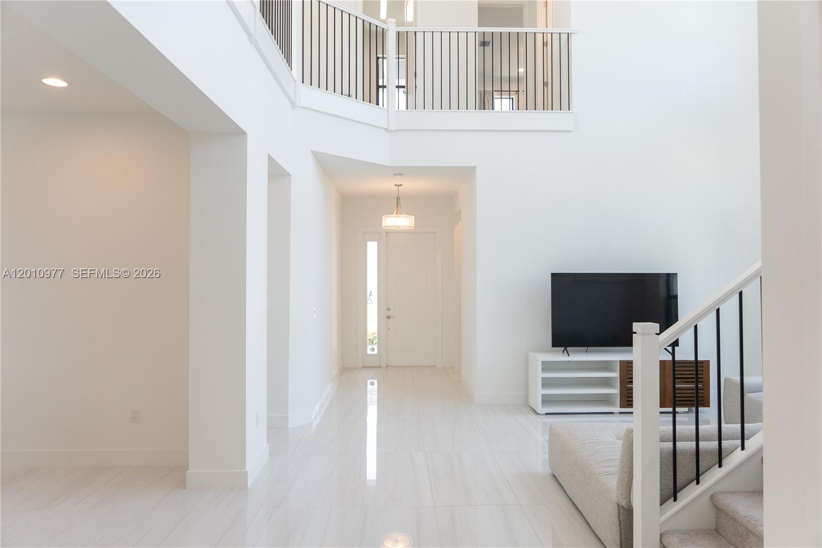 A bright, two-story entryway features white walls, tile flooring, and a staircase with metal railings — 8151 Laurel Falls Dr, Boca Raton FL 33496, BOCA RATON, FL