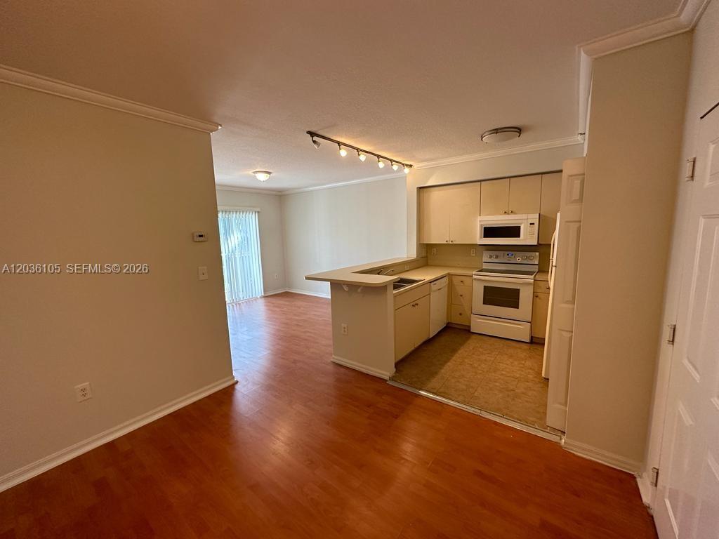 An open-concept kitchen with white appliances overlooks a living area with wood-look flooring — CUTLER BAY, FL