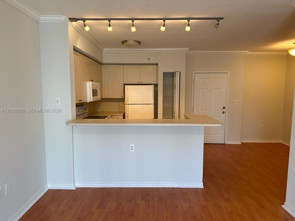 A kitchen with white cabinets and appliances overlooks a living area with wood flooring — CUTLER BAY, FL