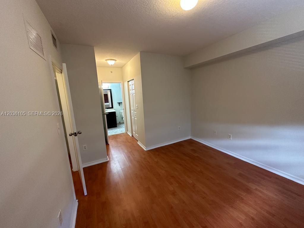 An empty room features wood-look flooring, light-colored walls, and a doorway leading to a bathroom — CUTLER BAY, FL
