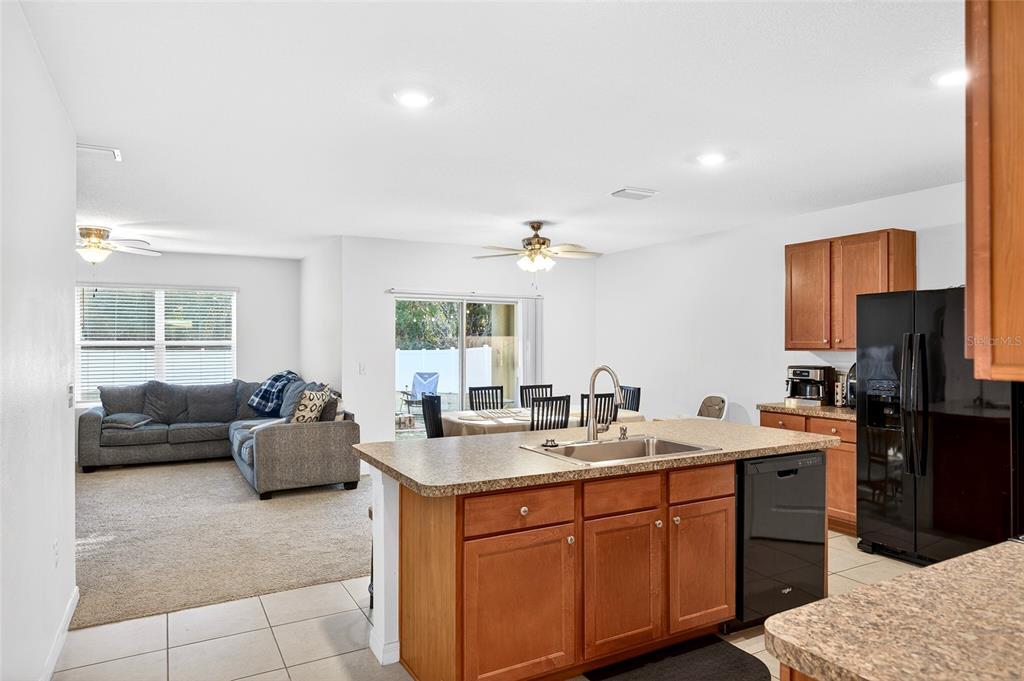 A kitchen with wood cabinets and a sink island overlooks an open living and dining area — 2530 NE 42ND ROAD, OCALA, FL