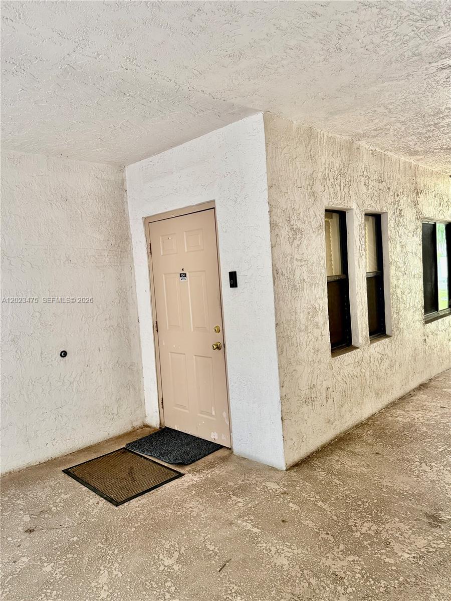 A beige door with a doormat sits on a textured white exterior wall — 4725 SW 62nd Ave # 104, Davie FL 33314, DAVIE, FL