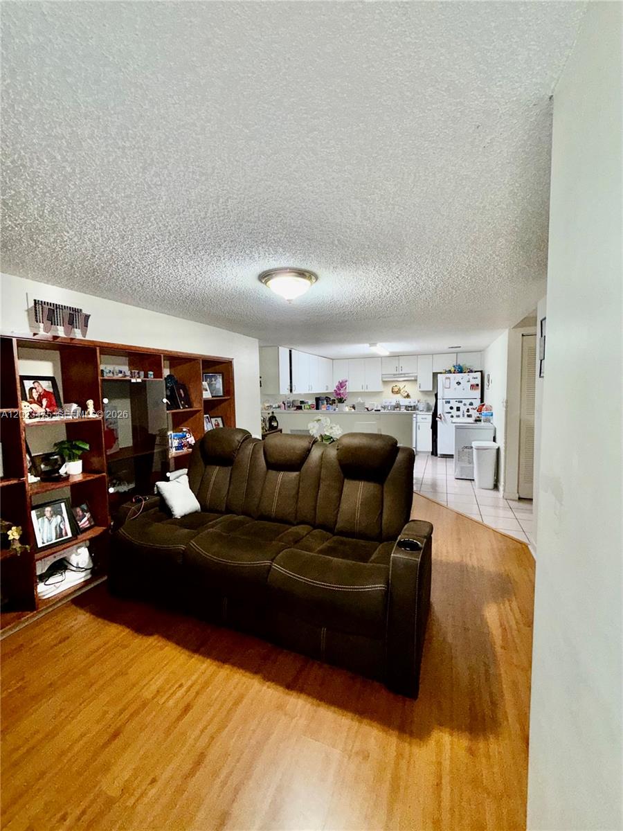 A living room with a brown reclining sofa and wooden shelving faces an open kitchen — 4725 SW 62nd Ave # 104, Davie FL 33314, DAVIE, FL