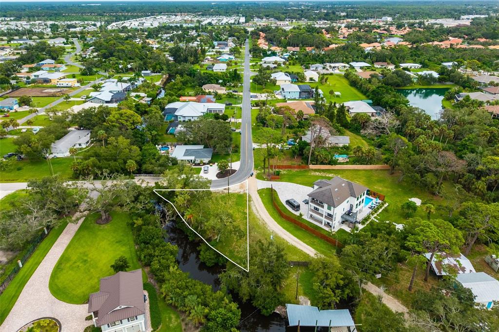 An aerial view shows a vacant, triangular-shaped lot situated between two houses and a canal — OAK STREET, NOKOMIS, FL