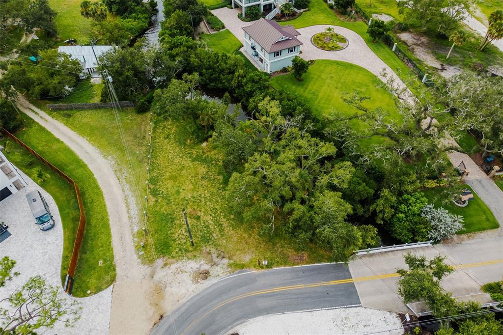 An aerial view shows a vacant grassy lot bordered by trees, a road, and nearby houses — OAK STREET, NOKOMIS, FL