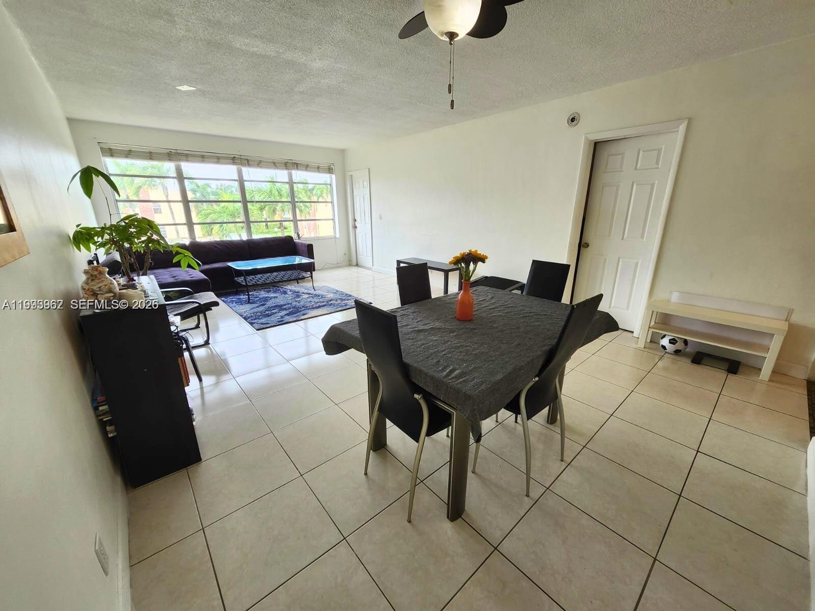 An open-concept living and dining area features white tile floors and a large window — 851 NE 14th Ave # 420, Hallandale Beach FL 33009, HALLANDALE BEACH, FL