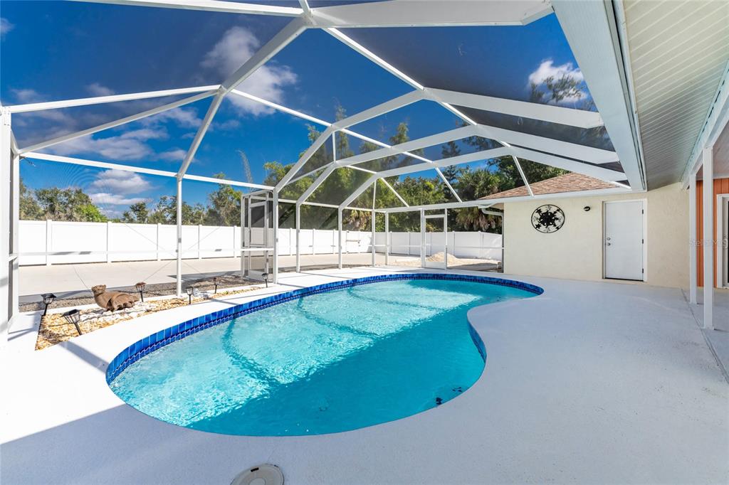 A swimming pool with blue tile trim sits inside a screened-in patio enclosure — 1600 THOMAS STREET, ENGLEWOOD, FL