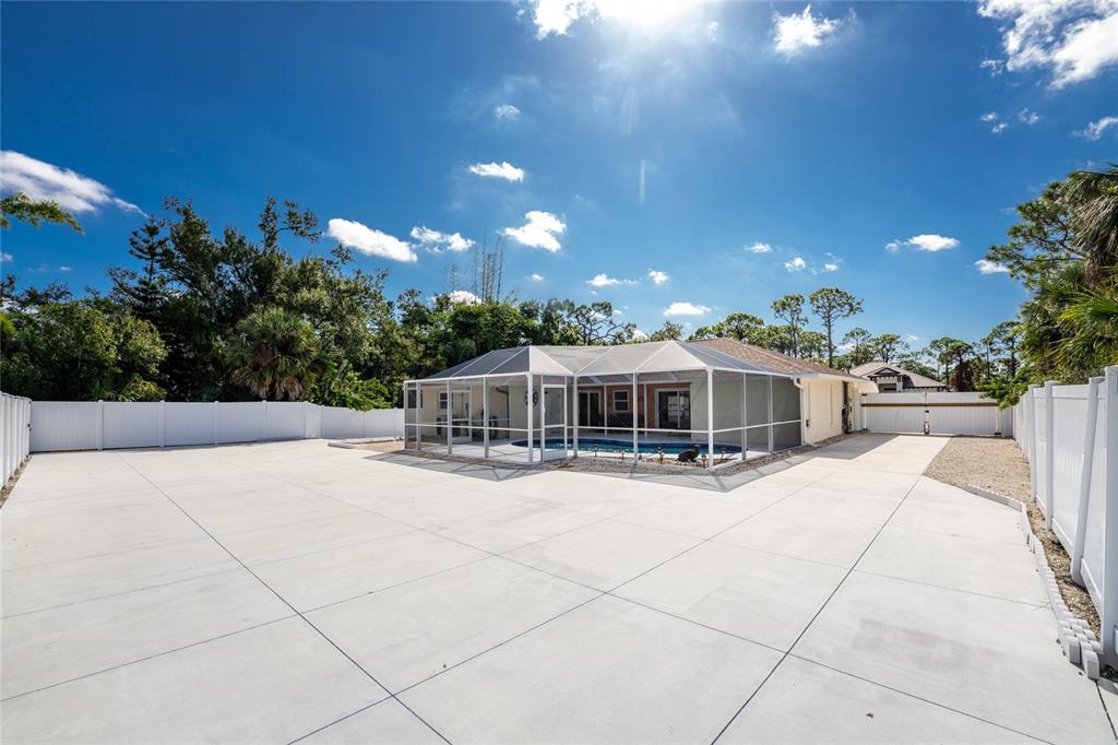A backyard features a large concrete patio, a screened-in swimming pool, and white vinyl fencing — 1600 THOMAS STREET, ENGLEWOOD, FL