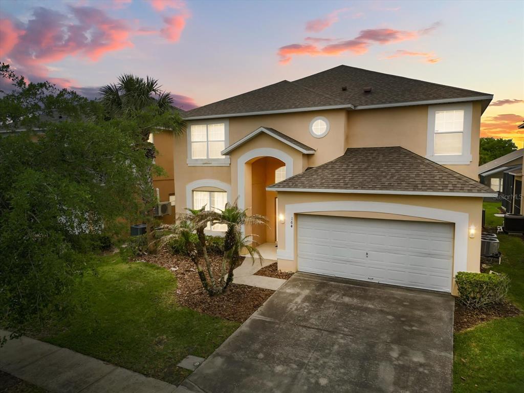 A two-story tan stucco house with a two-car garage and a concrete driveway — 164 CASTAWAY BEACH WAY, KISSIMMEE, FL