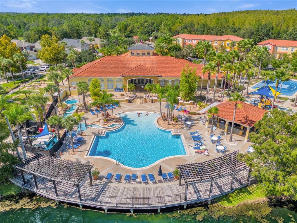 An aerial view of a community pool area with a clubhouse, deck, and surrounding trees — 164 CASTAWAY BEACH WAY, KISSIMMEE, FL