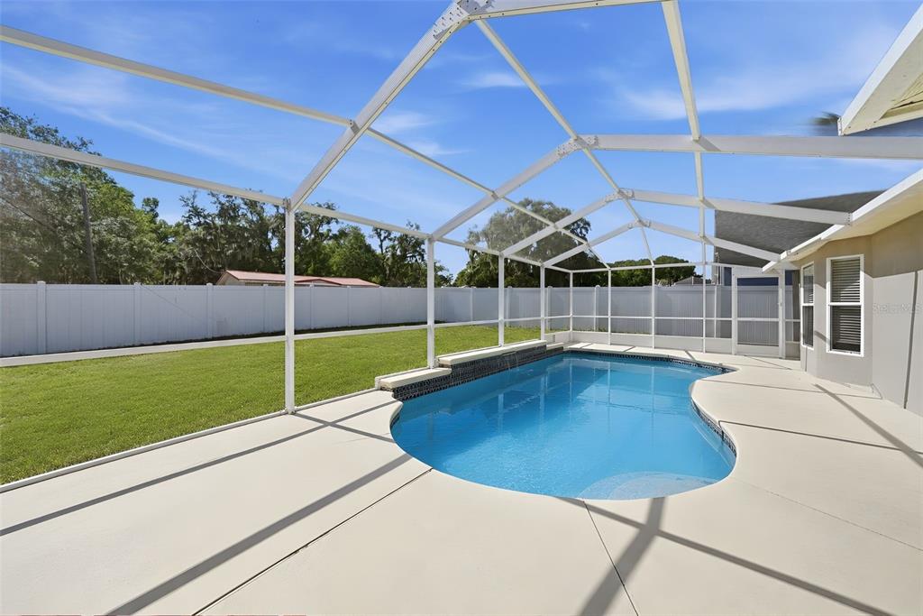A backyard features a swimming pool enclosed by a white screen cage and vinyl fencing — 3511 GRAY WHETSTONE STREET, BRANDON, FL