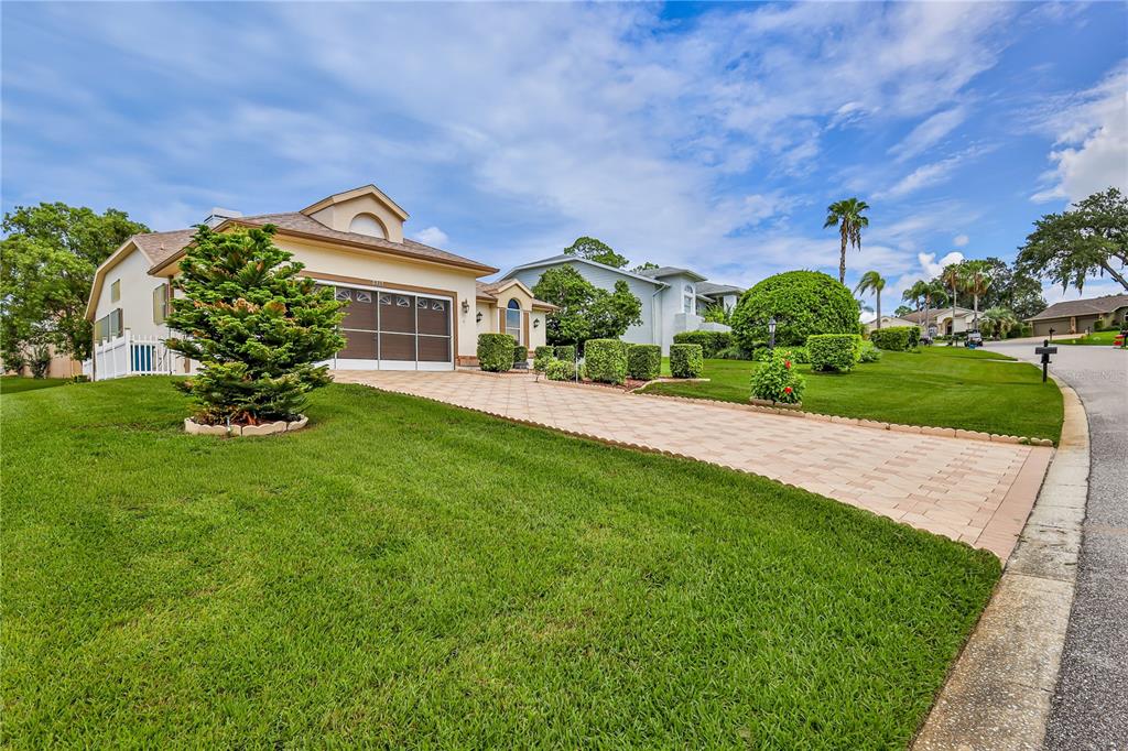 A single-story house with a paved driveway, manicured lawn, and a garage with a screen door — 2317 SCENIC HILL DRIVE, SPRING HILL, FL