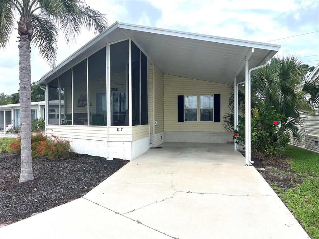 A light-colored mobile home features a screened-in porch, a carport, and a concrete driveway — 817 S GREEN CIRCLE, VENICE, FL