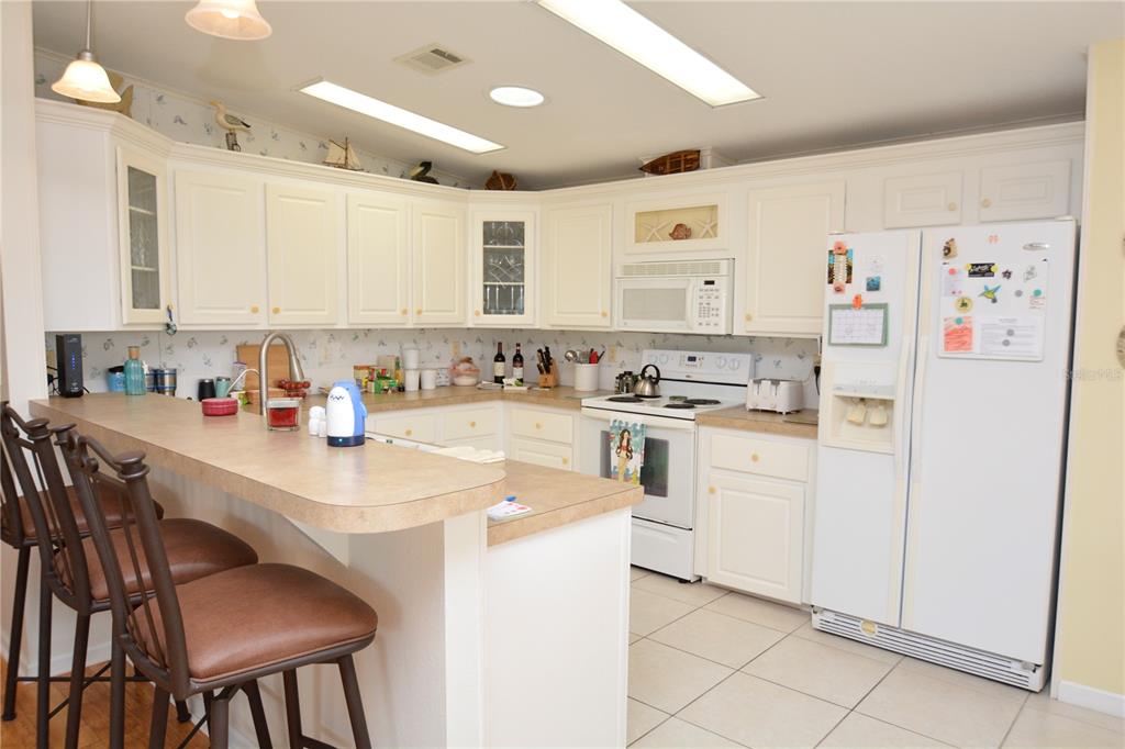 A kitchen features white cabinets, laminate countertops, a breakfast bar, and white appliances — 817 S GREEN CIRCLE, VENICE, FL