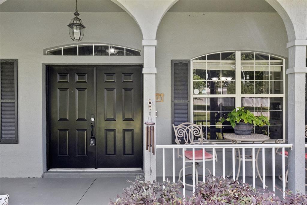 A covered front porch features a black double door, arched columns, and a small bistro set — 31038 FAIRVISTA DRIVE, TAVARES, FL