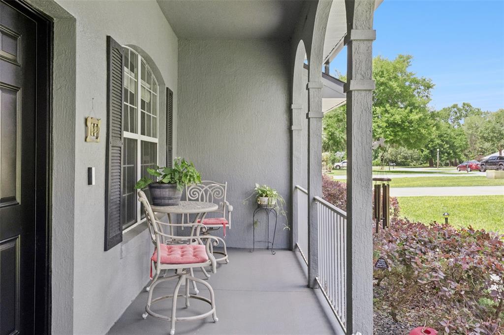 A covered front porch features gray stucco walls, arched columns, and a small bistro set — 31038 FAIRVISTA DRIVE, TAVARES, FL